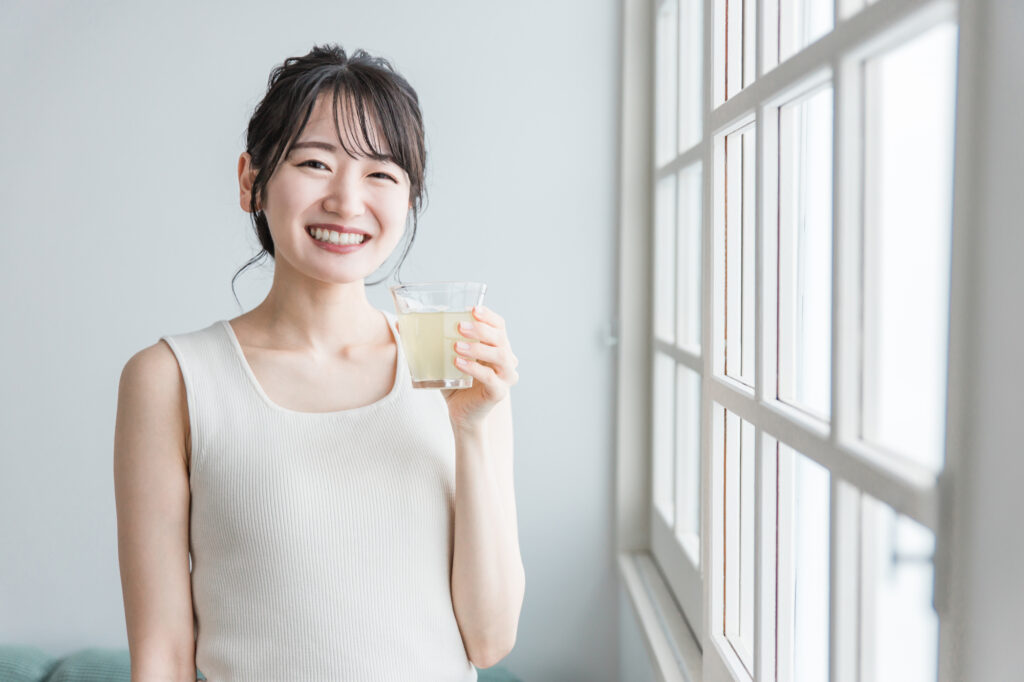 窓際でコップに入った飲み物を持つ女性