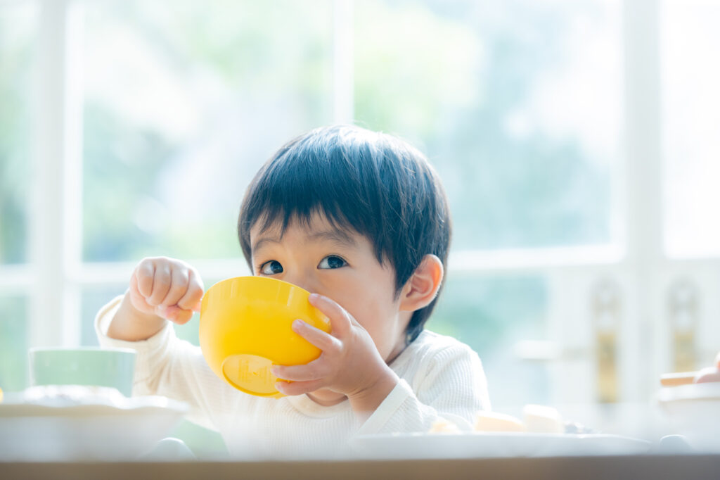 小さい男の子が黄色いお茶碗を持って食べも物をかき込む