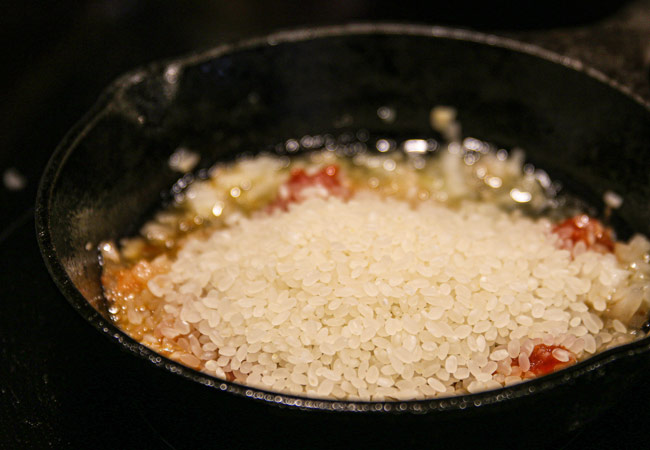 みじん切りにした玉ねぎとにんにく、ダイストマトを混ぜ、米を入れて炒める