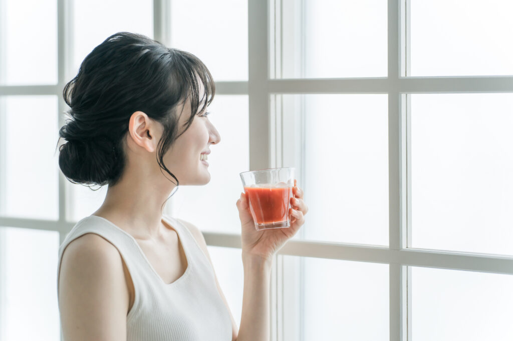 窓際でトマトジュースを飲む女性